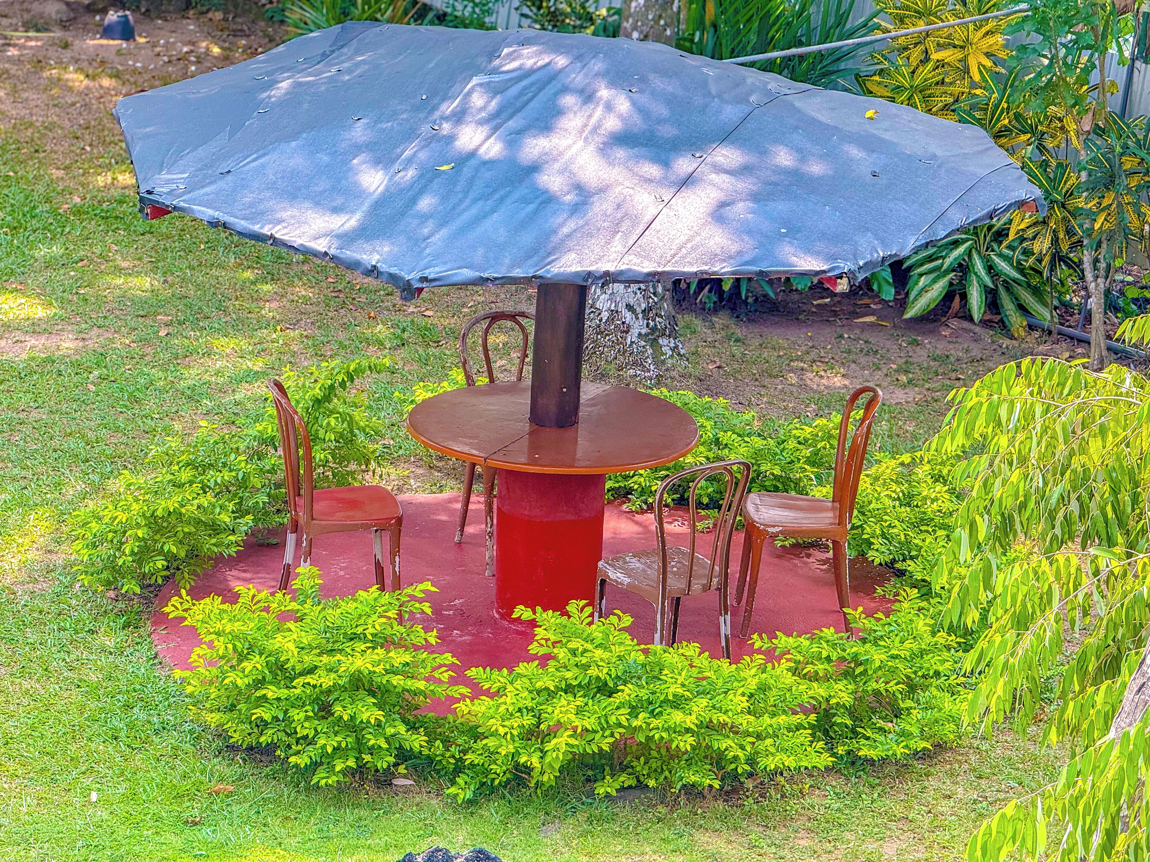 A round table with four chairs, a red base, and a large umbrella overhead.