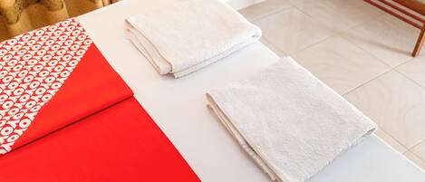 Una habitación ordenada con una mesa blanca, dos toallas blancas dobladas, un mantel de mesa con estampado rojo y blanco, y un banco de madera.