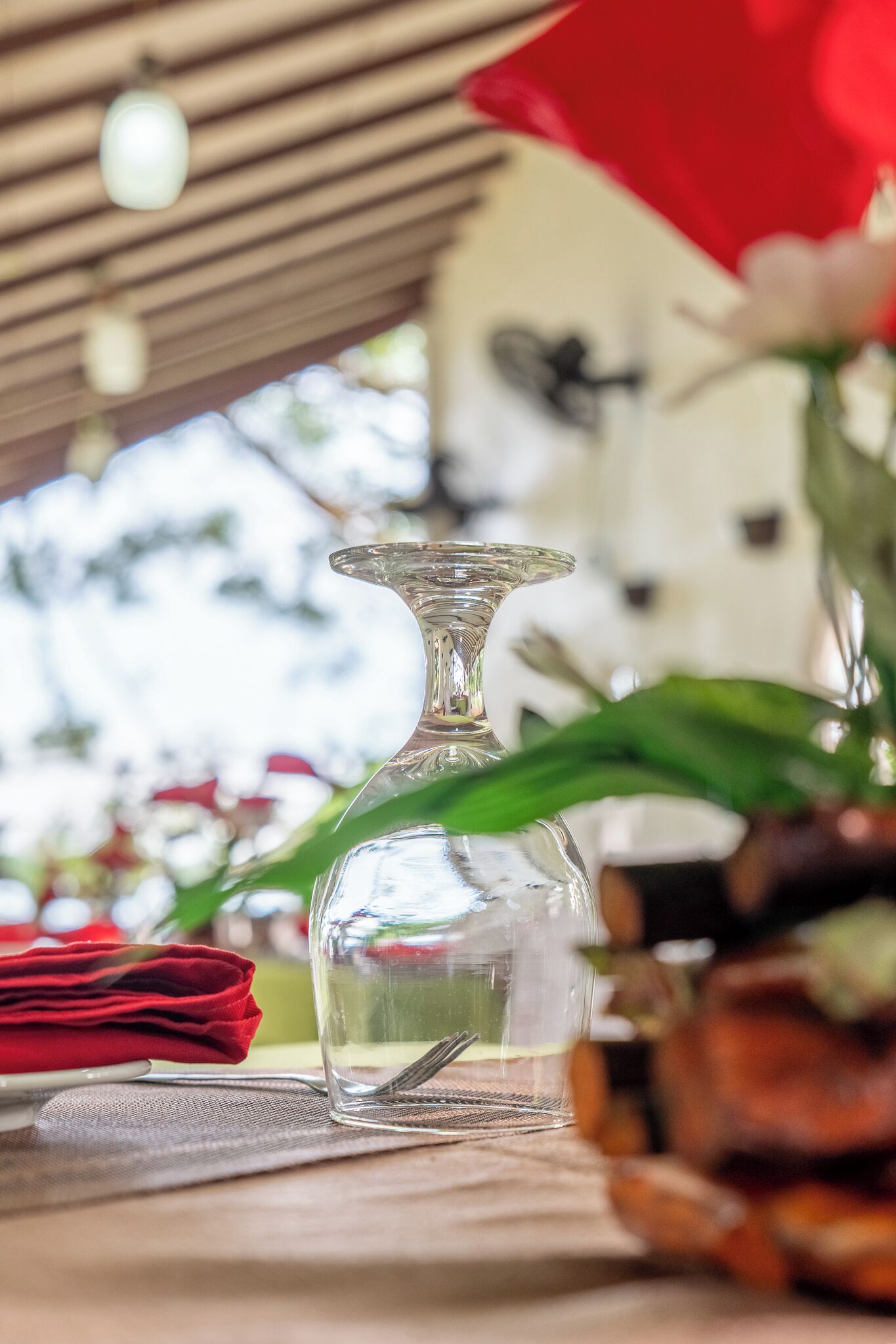 Un vase en verre transparent est posé sur une table, accompagné d’une serviette rouge et d’une cuillère, sous une structure en bois ornée de luminaires suspendus.