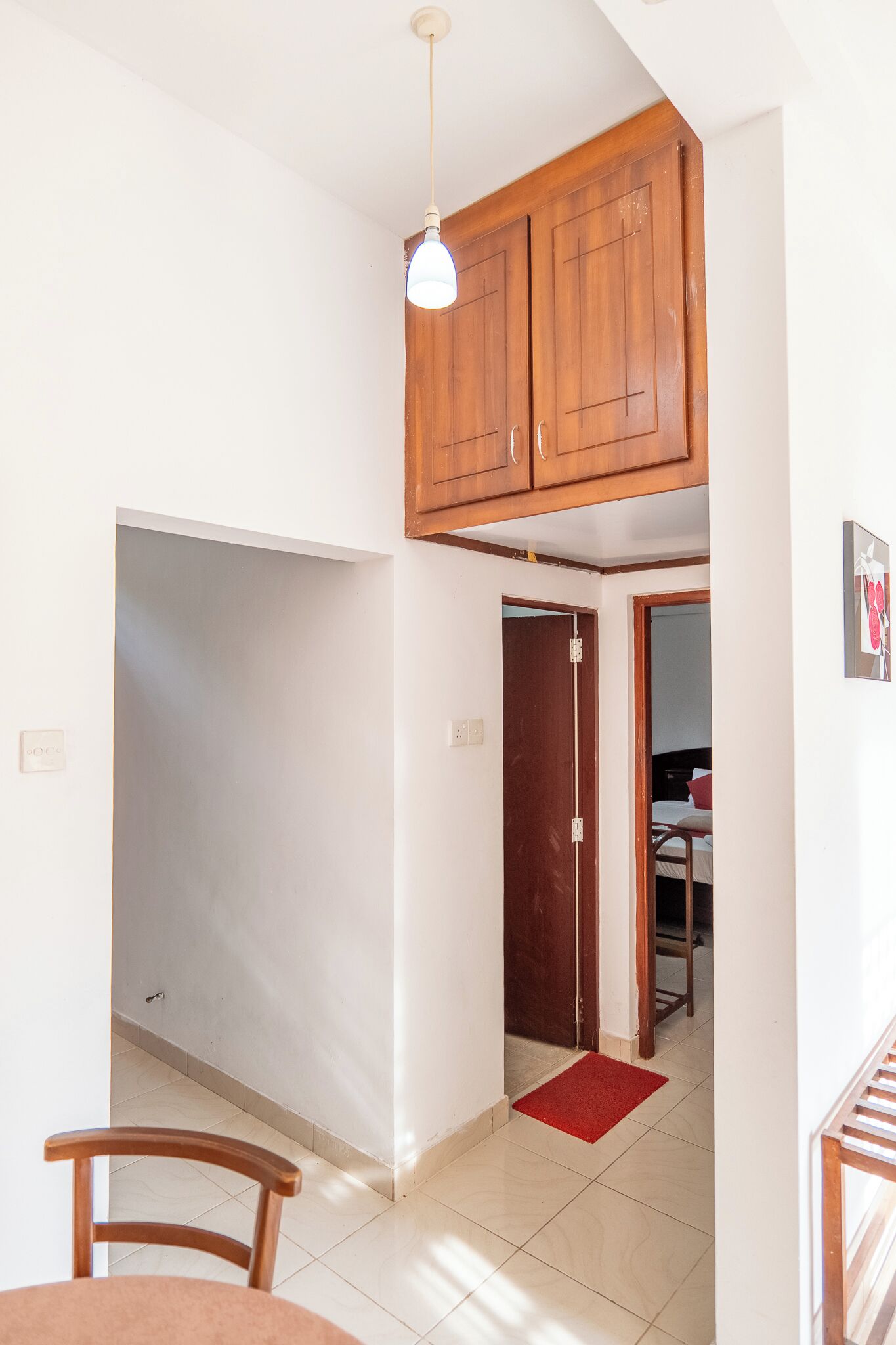 A room with a wooden ceiling, a dining table, a chair, a red rug, and a door leading to another room.