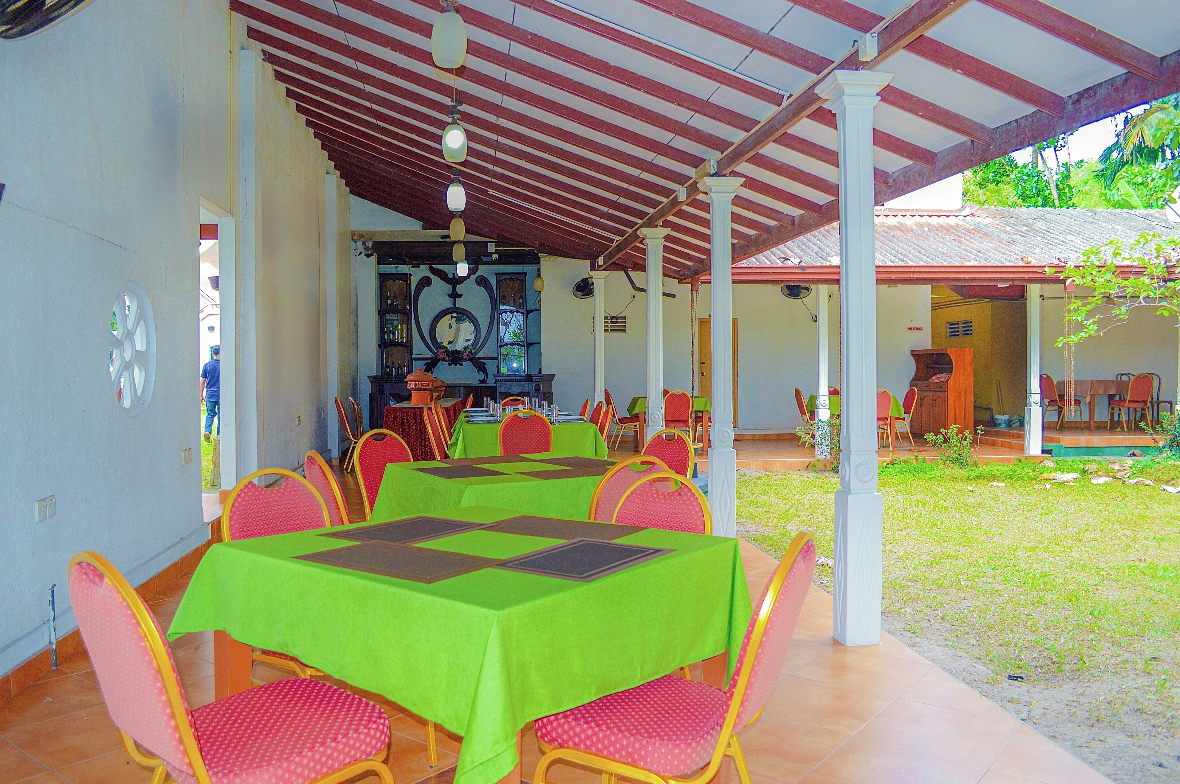 A covered outdoor dining area with tables and chairs, a clock, and a view of a house in the background.
