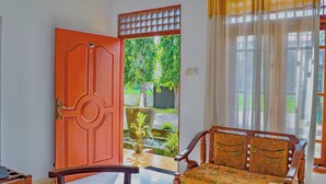 Puerta abierta que da a un jardín con una fuente, un banco de madera y una ventana con cortinas.