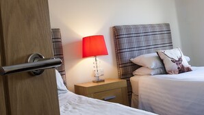A hotel room with a wooden door, a bedside table with a red lamp, a plaid headboard, and a bed with a pillow. - Riverside Apartments (Wick)