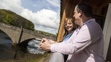 A man and a woman sitting by a river with a bridge in the background.