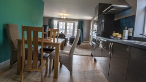 A modern kitchen with wooden chairs, a dining table, and a view of the city through large windows. - Riverside Apartments (Wick)