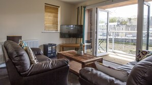 A living room with a sofa, a coffee table, a TV, and a window with blinds. - Riverside Apartments (Wick)