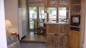 Una cocina compacta con refrigerador, una barra de madera con taburetes y un televisor.