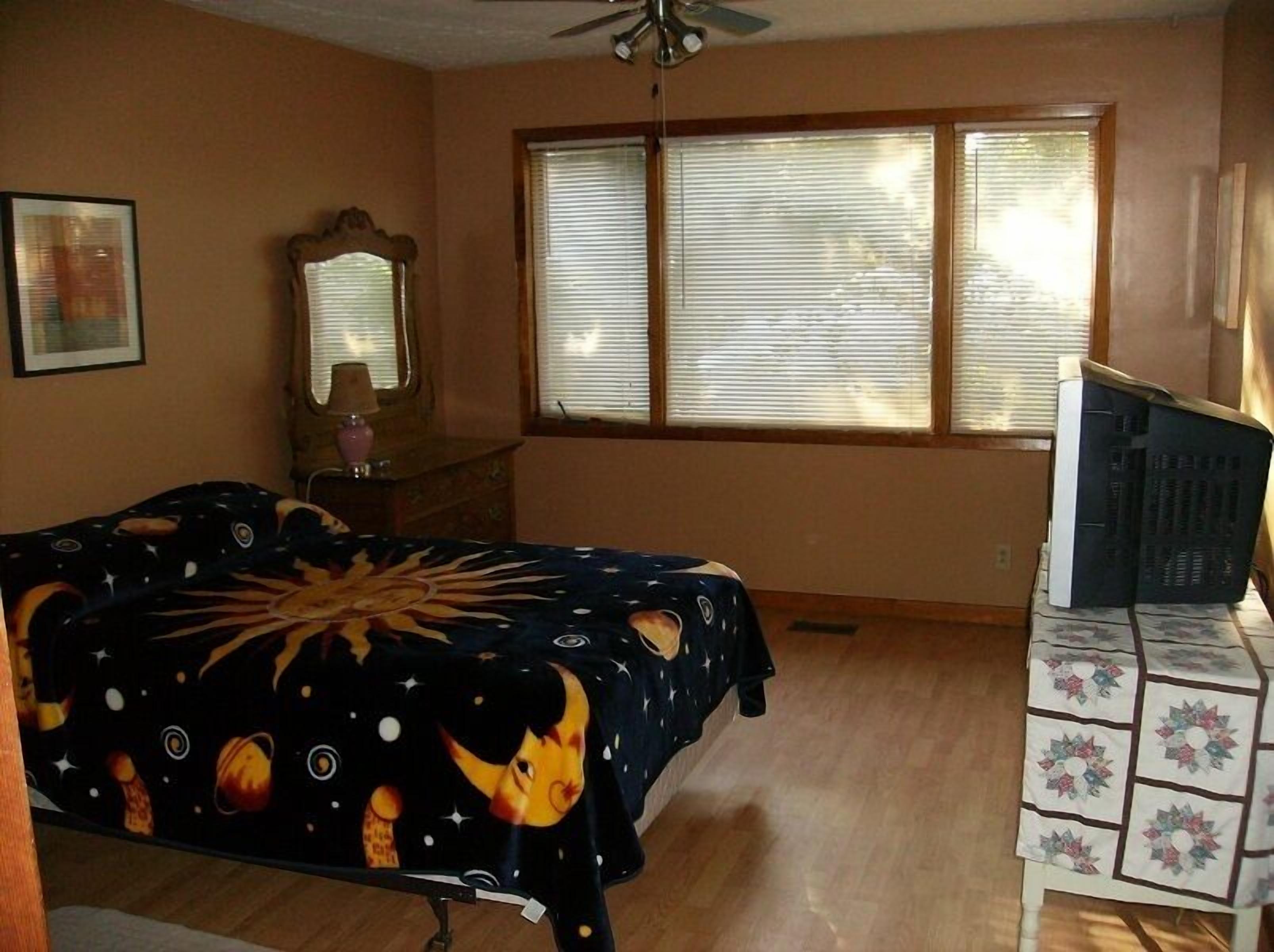 A bedroom with a bed, a dresser, a mirror, and a window with blinds.