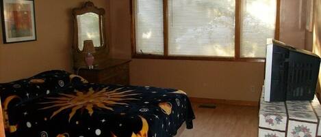A bedroom with a bed, a dresser, a mirror, and a window with blinds.