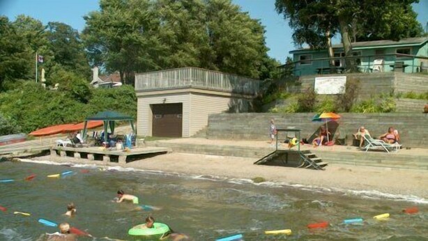 Una piscina con gente usando dispositivos flotantes, una torre de salvavidas y un edificio pequeño al fondo.