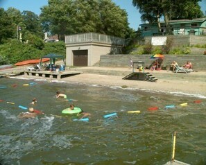 Une piscine où des personnes utilisent des bouées, une tour de surveillance pour les sauveteurs et un petit bâtiment en arrière-plan.