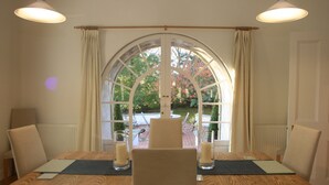 Mesa de jantar com duas cadeiras, janela com cortinas e duas luminárias pendentes.