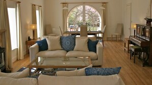 Uma sala de estar com sofá, mesa de centro, piano e uma janela grande com cortinas.