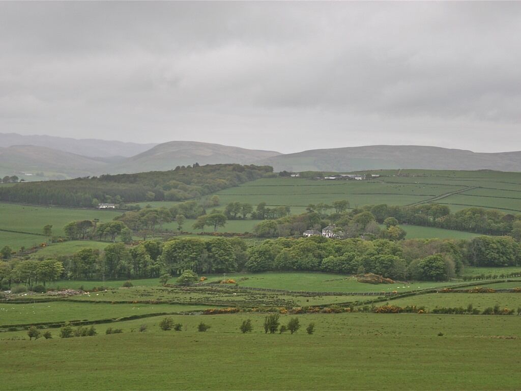Paisagem rural com colinas onduladas, árvores esparsas e alguns edifícios.