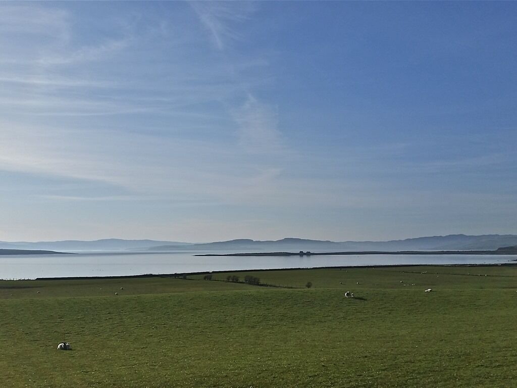 A wide-open grassy field with a body of water and distant mountains.