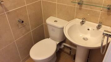 Un baño con inodoro y lavabo, azulejos color beige y una repisa de vidrio sobre el lavabo.