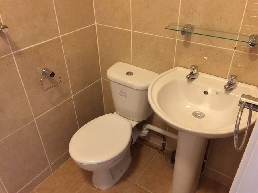 Un baño con inodoro y lavabo, azulejos color beige y una repisa de vidrio sobre el lavabo.