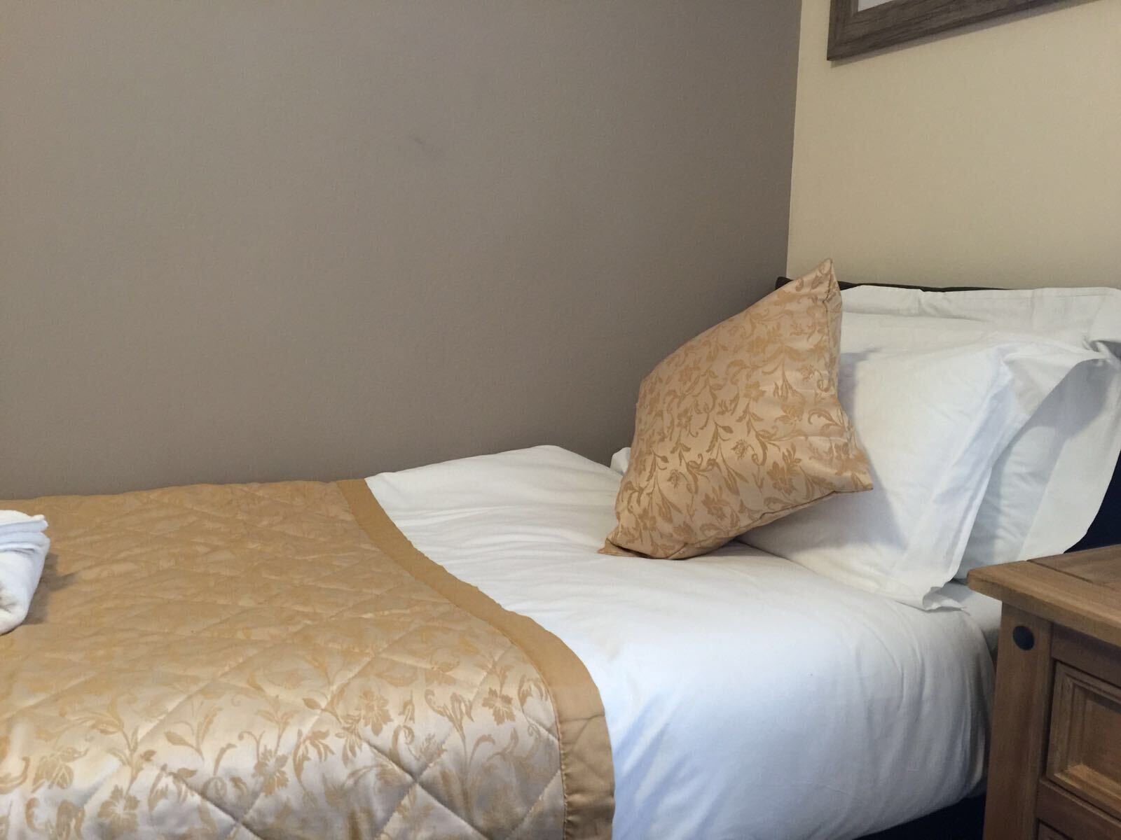 Una cama bien hecha con una colcha color beige y una única almohada decorativa.