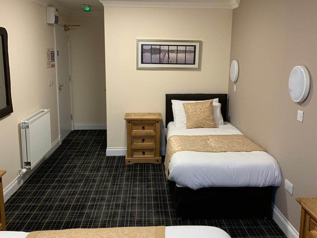 A hotel room with a bed, a bedside table, a radiator, and a picture on the wall.