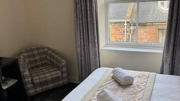 A hotel room with a bed, a plaid armchair, and a window with a view of buildings.