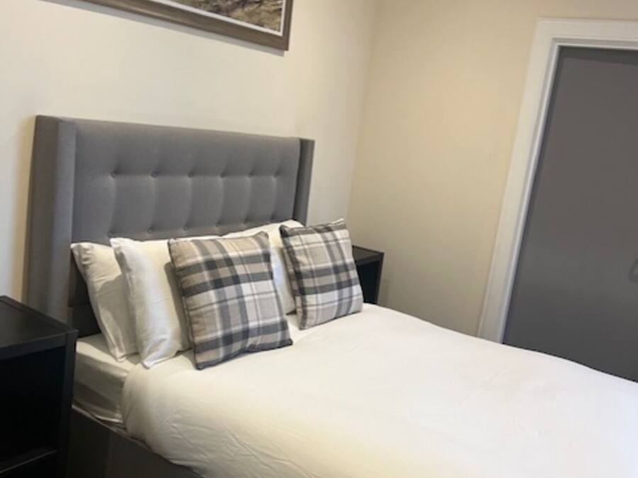 A bedroom with a bed, a headboard, a nightstand, a door, and a painting on the wall.