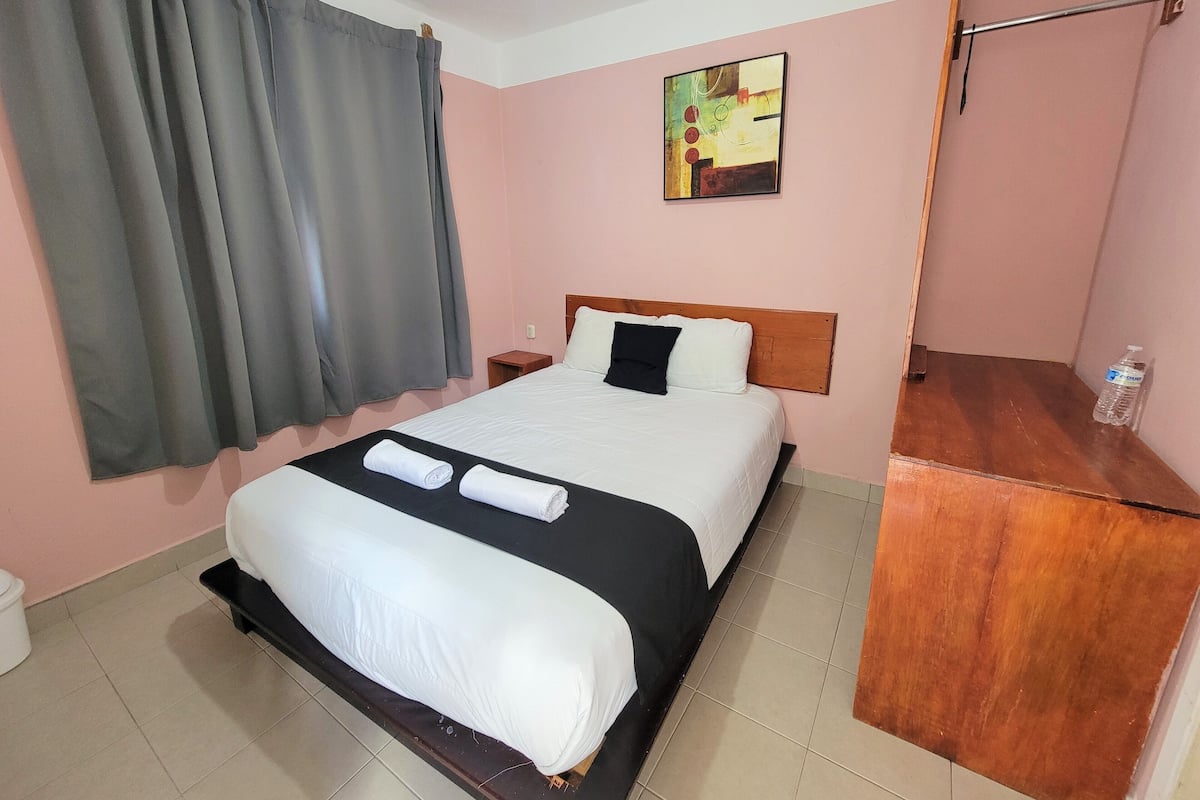 A hotel room with a bed, a nightstand, a painting on the wall, and a window with curtains.