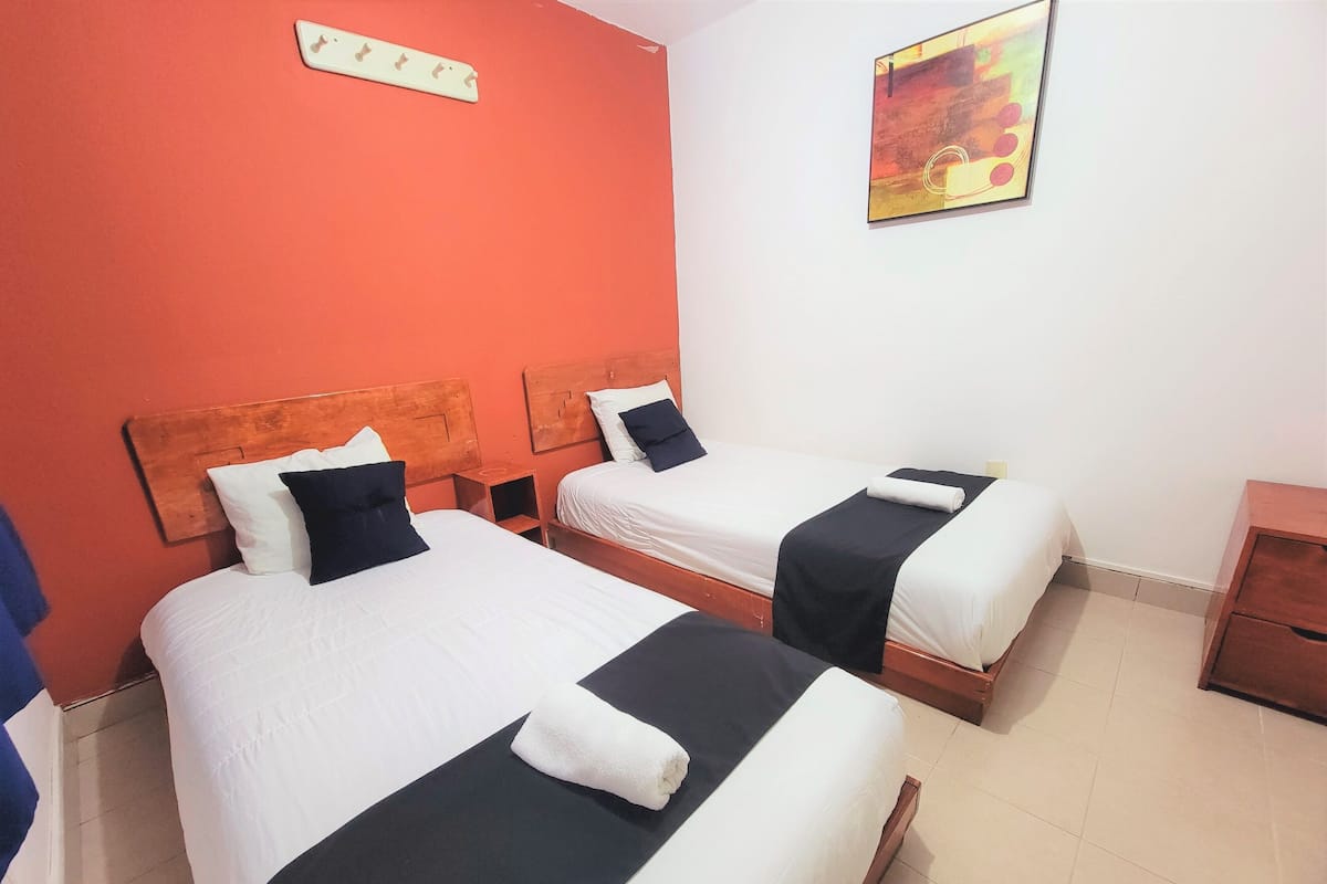 A hotel room with two beds, each with white linens and black bedspreads. There is a wooden headboard, a small wooden nightstand, and a wall-mounted artwork.