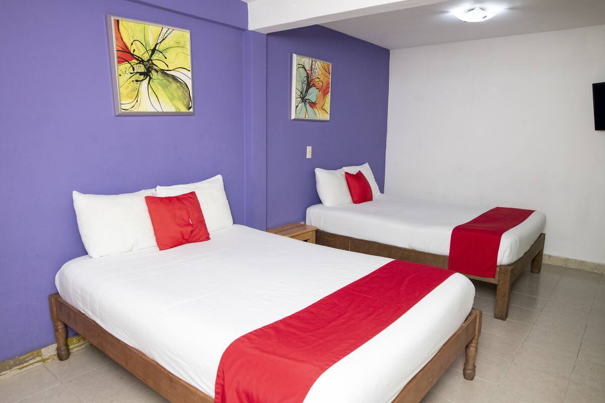 Two single beds with white and red bedding, purple walls, and two abstract paintings.