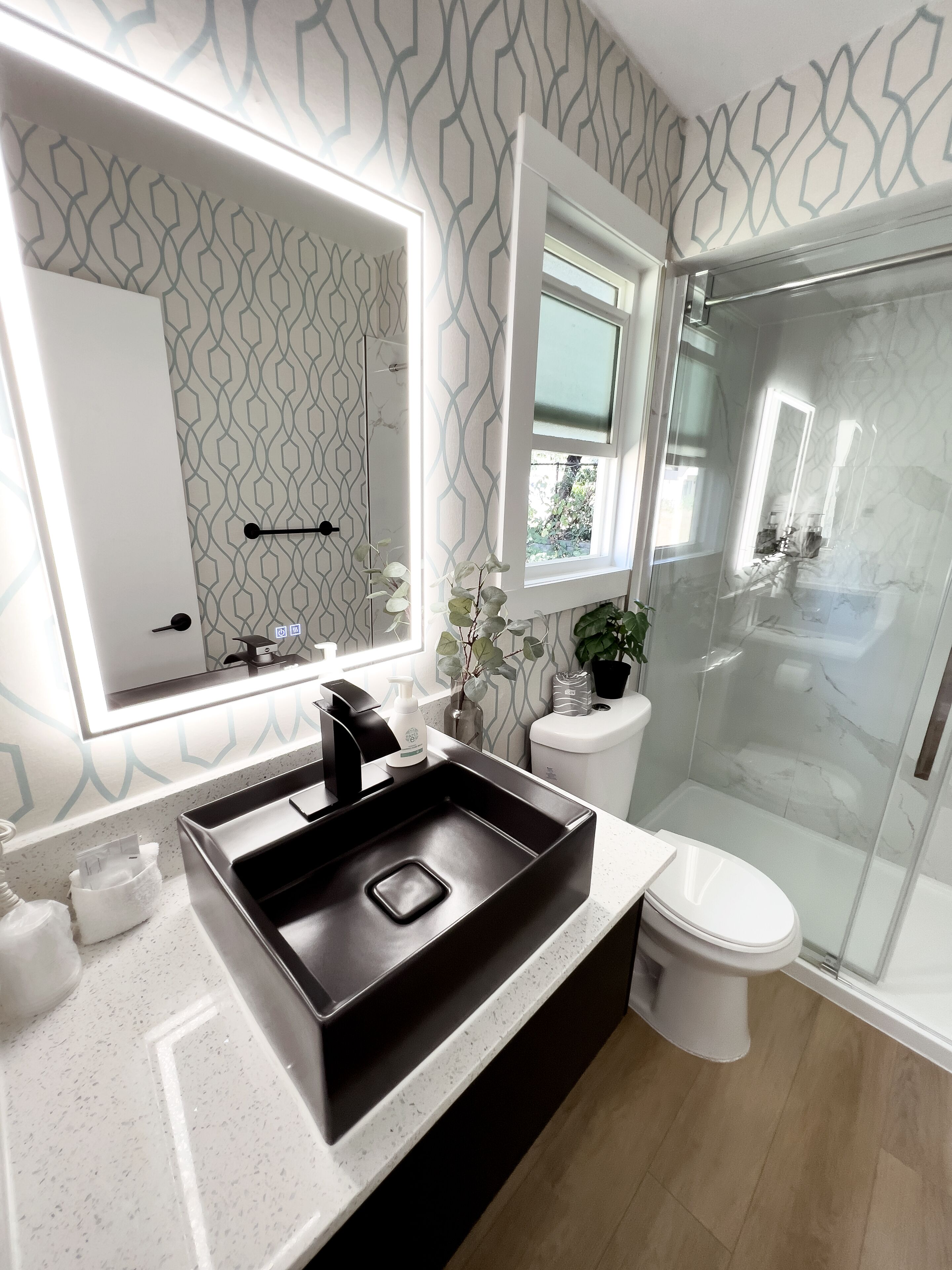 A modern bathroom with a large mirror, a black sink, a toilet, and a glass shower enclosure.