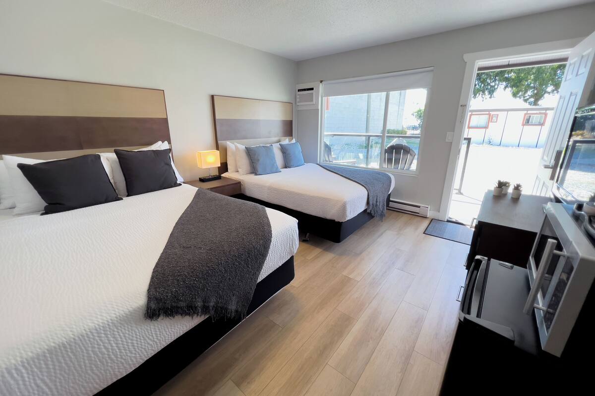 A hotel room with two beds, a desk, a chair, a window with a view, and a door leading outside.