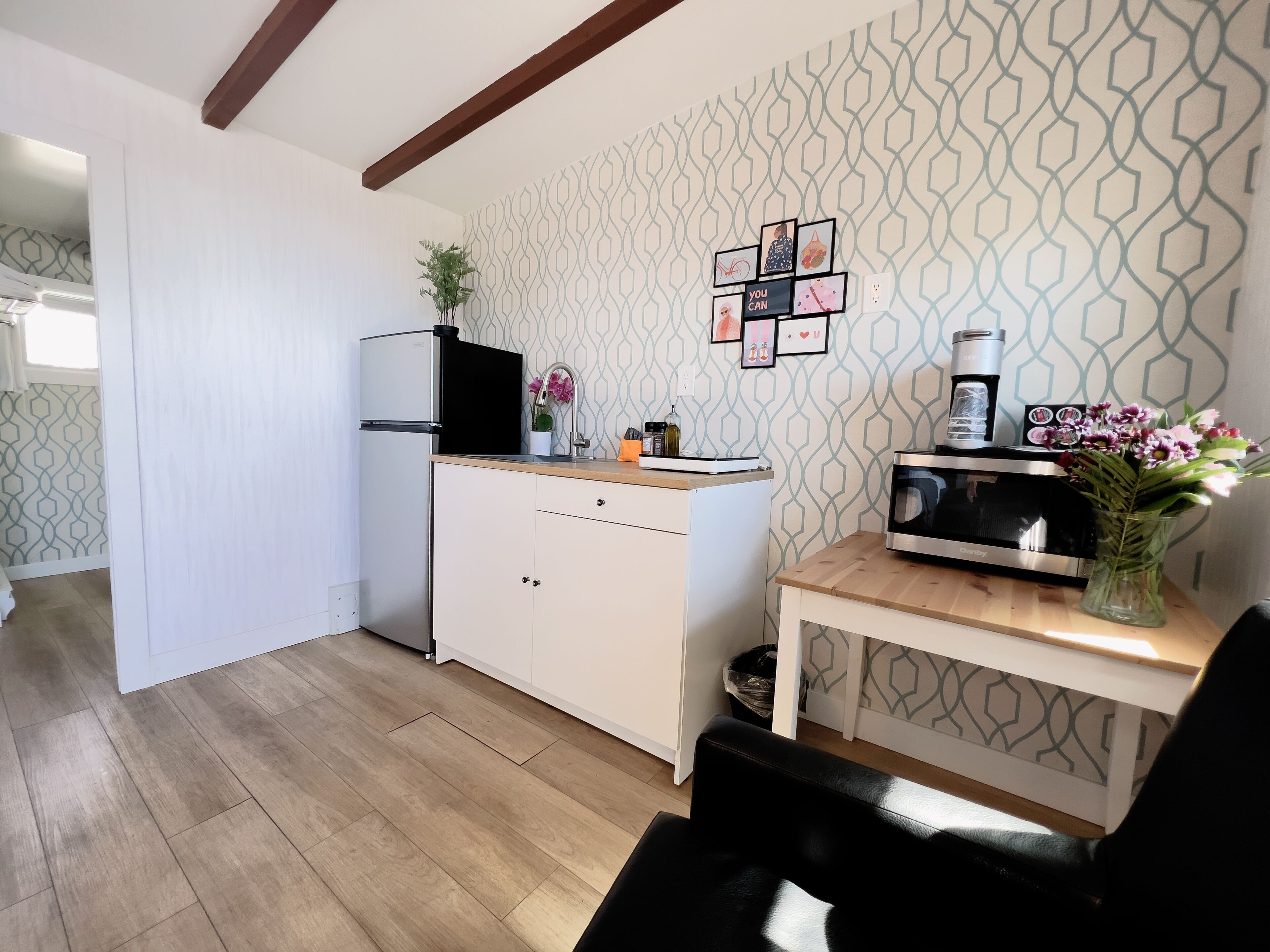 Cocina compacta con refrigerador, microondas y una pequeña mesa con un florero.