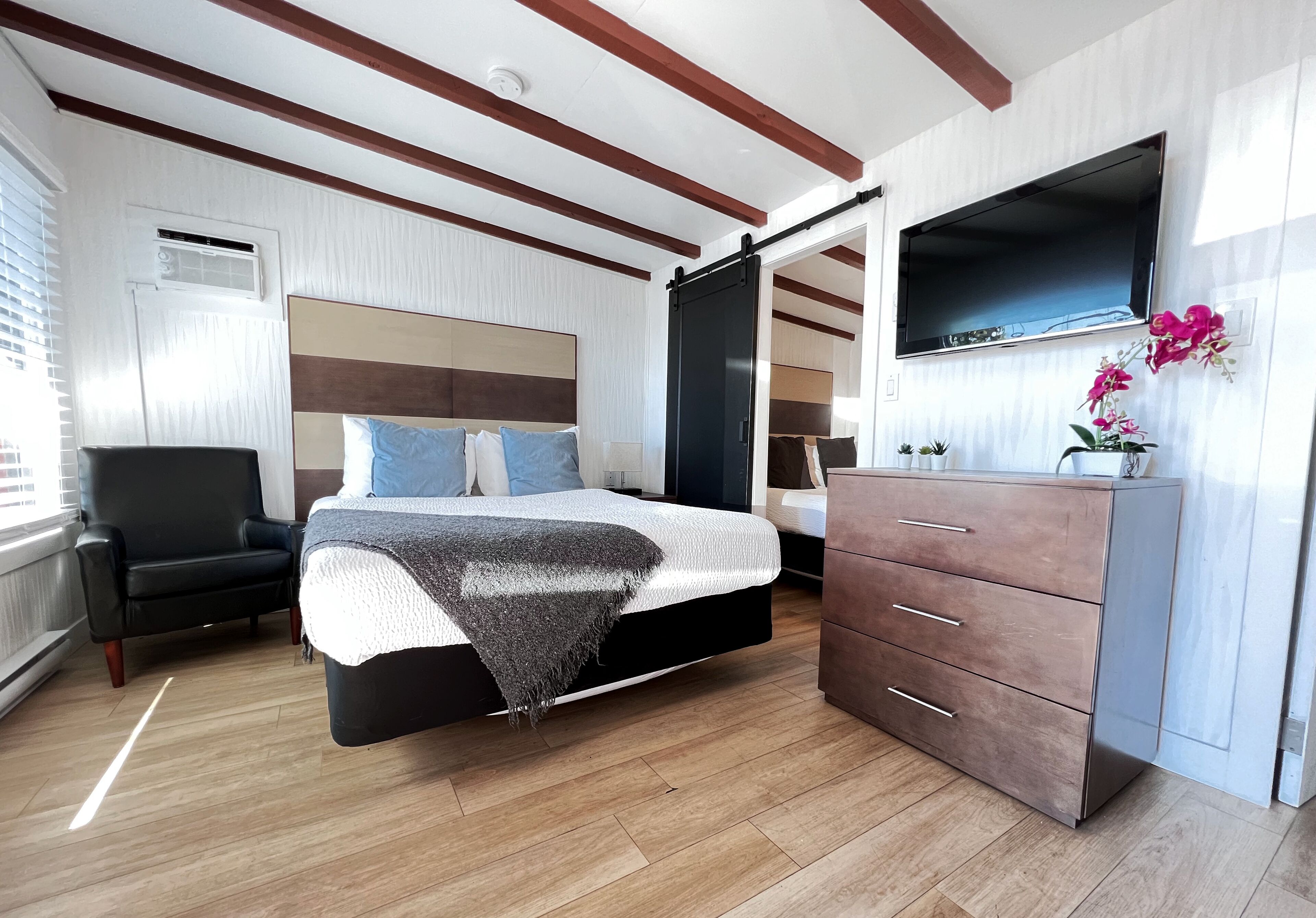 A bedroom with a bed, a chair, a dresser, and a TV mounted on the wall.