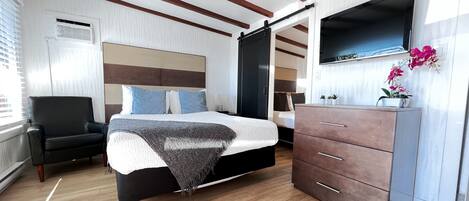 A bedroom with a bed, a chair, a dresser, and a TV mounted on the wall.