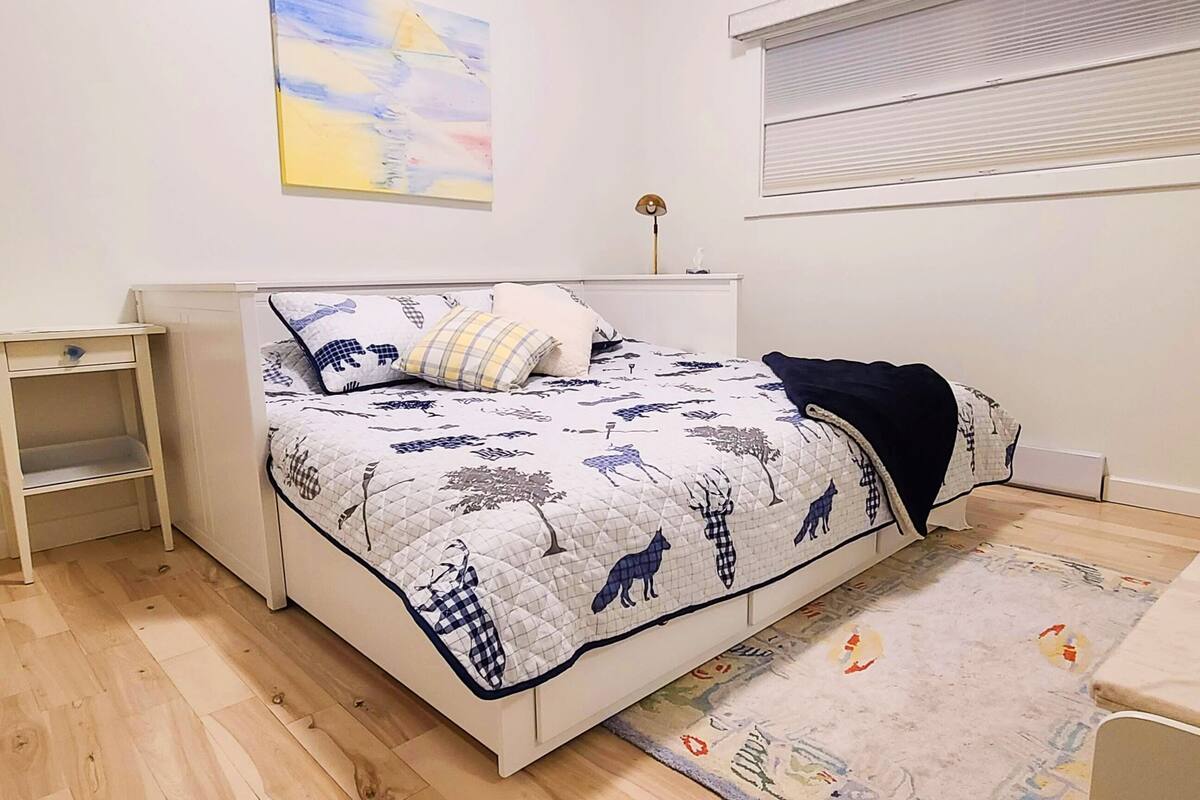 A bedroom with a bed, bedside table, and a window with blinds.
