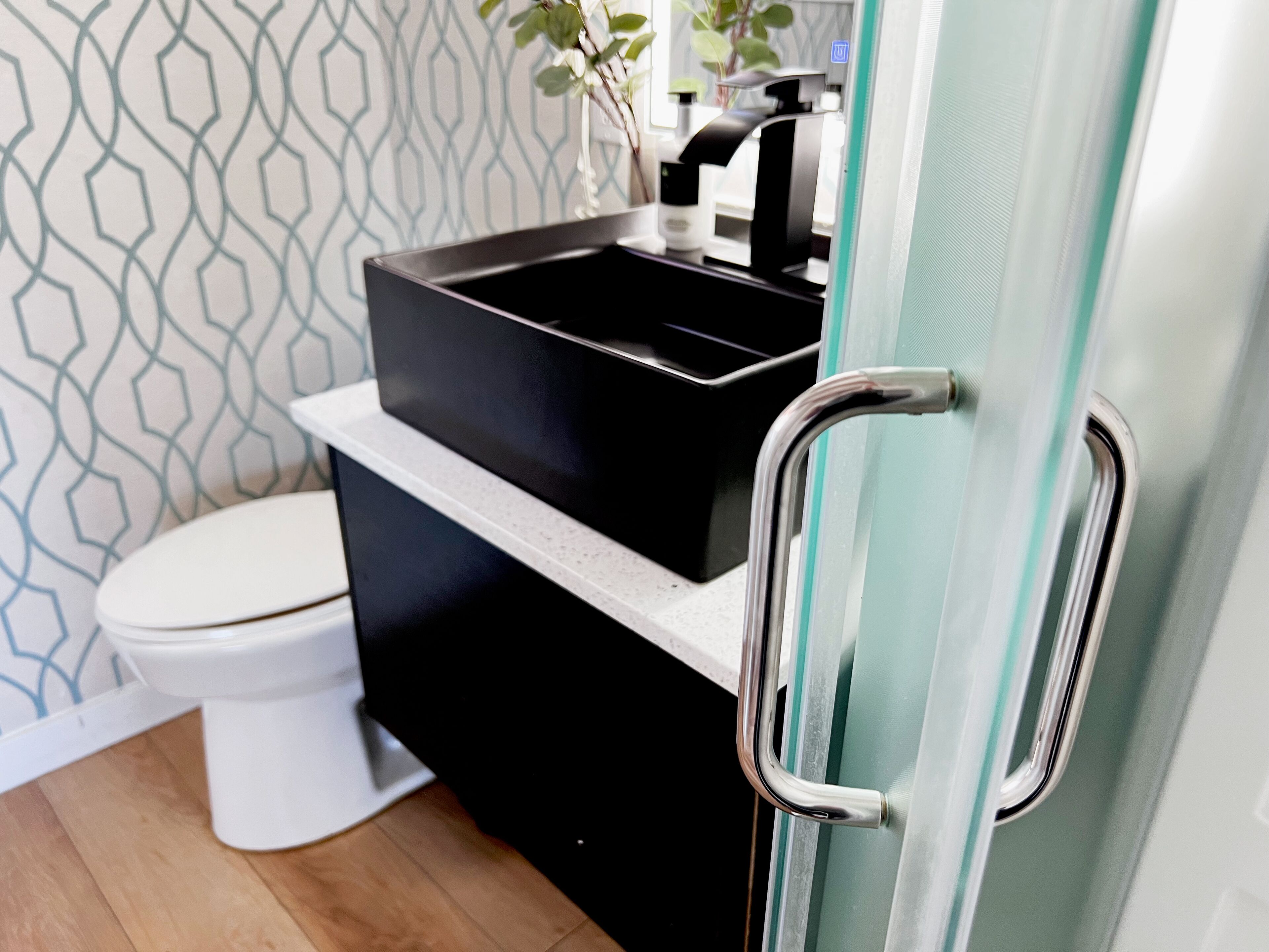 A bathroom with a toilet, a black sink, and a glass shower door.