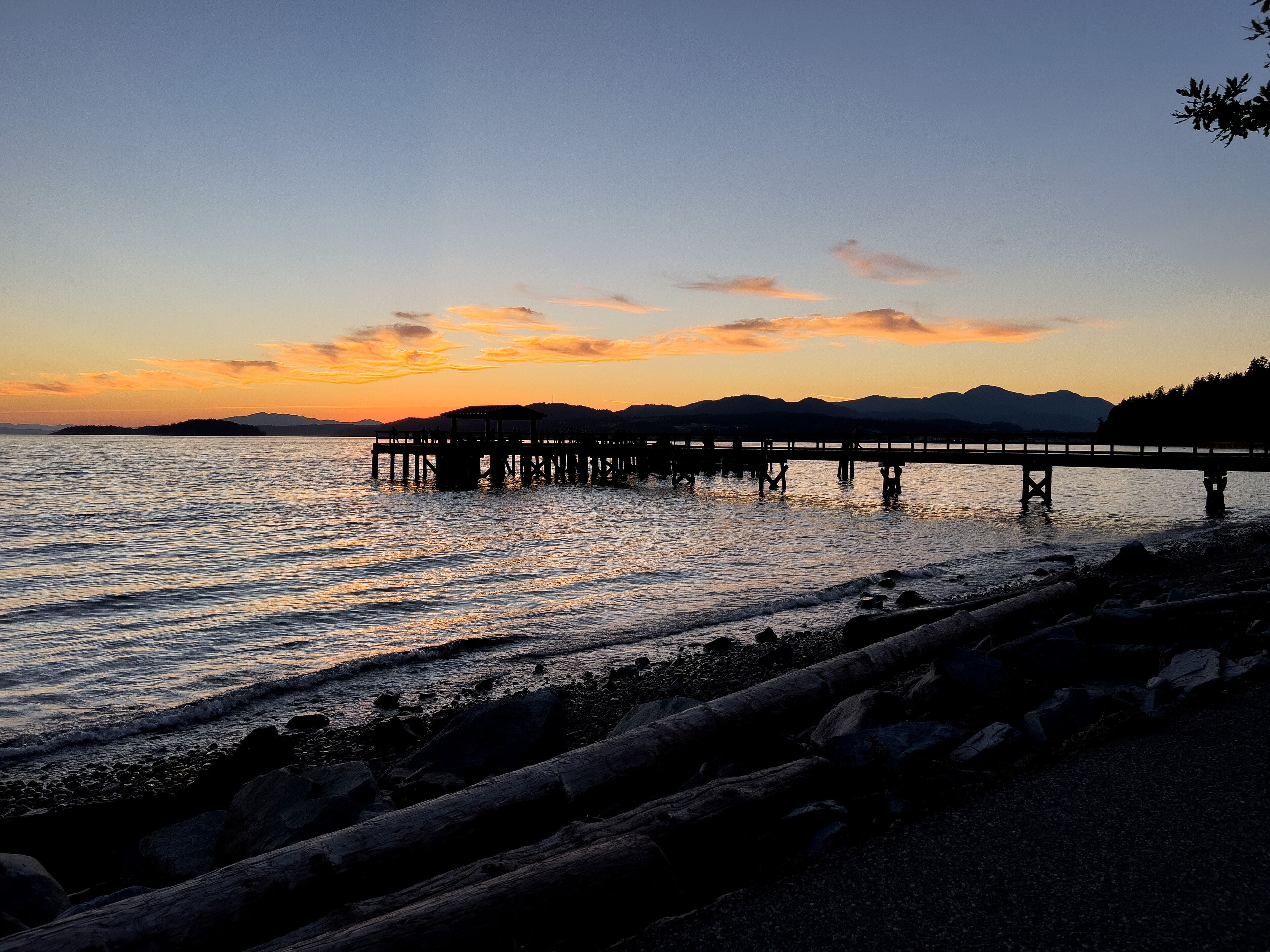 Un muelle se adentra en aguas tranquilas al atardecer, con montañas al fondo.