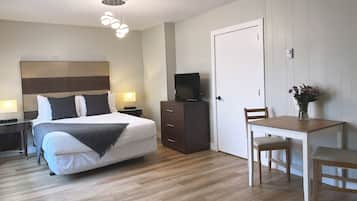Habitación de hotel con cama, mesita de noche, televisor, cómoda y una pequeña mesa de comedor con sillas.