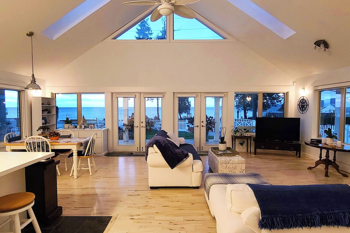 A spacious living area with a high ceiling, large windows, and a view of the sea.
