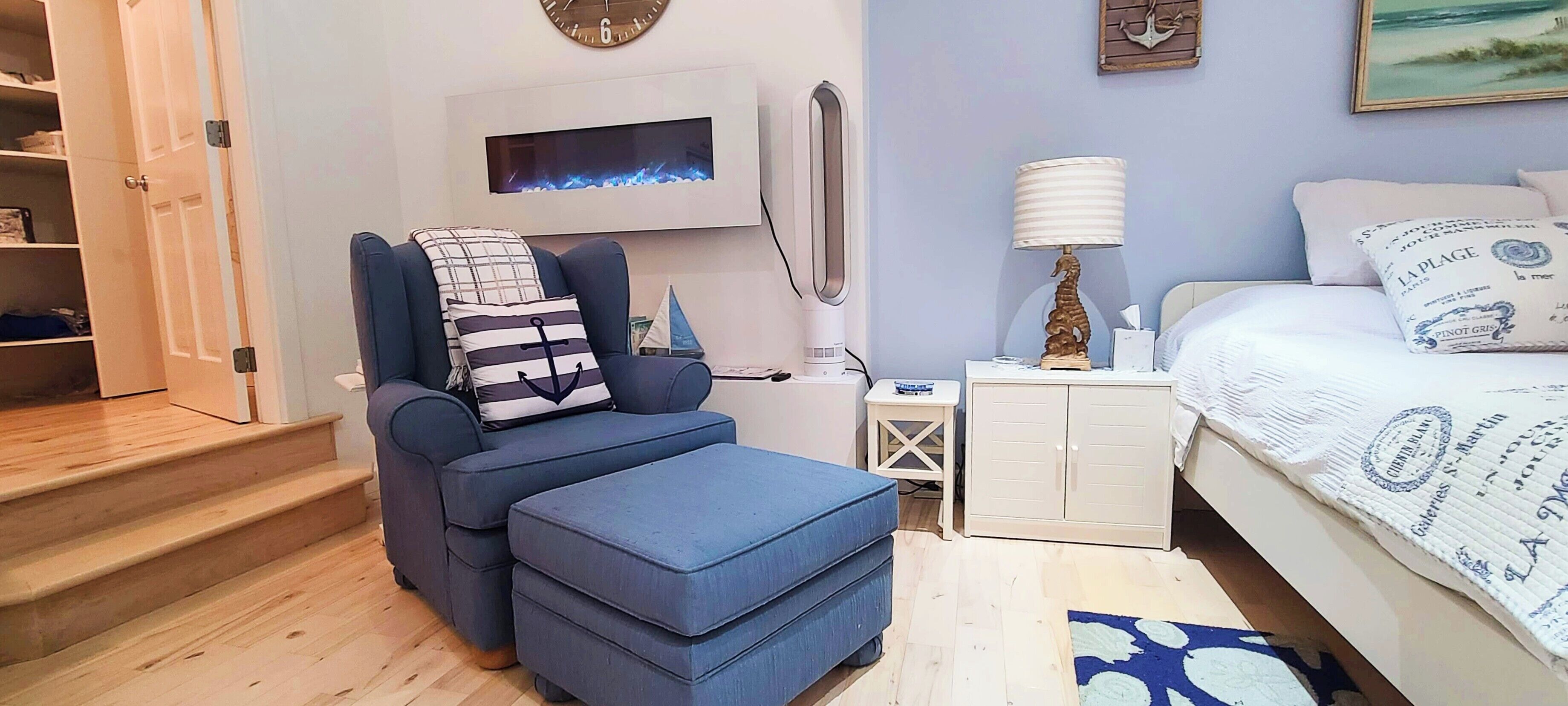 A bedroom with a bed, a blue sofa, a small table, a nightstand, a wall-mounted TV, and a door leading to a closet.