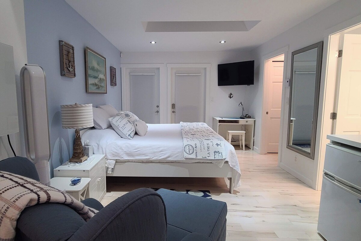 A bedroom with a bed, bedside tables, a TV, and a small kitchenette.