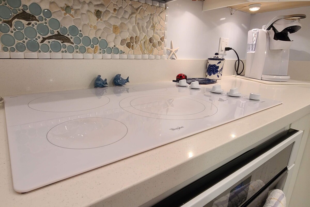 A kitchen with a white induction cooktop, a coffee maker, and a decorative backsplash.
