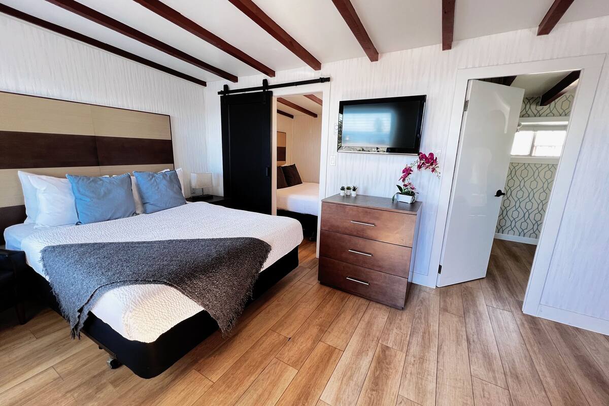 A bedroom with a bed, bedside table, dresser, TV, and a sliding door leading to another room.