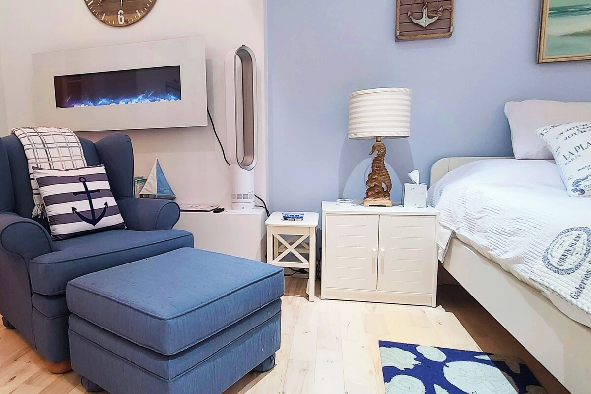 A bedroom with a bed, a blue sofa, a small table, a nightstand, a wall-mounted TV, and a door leading to a closet.