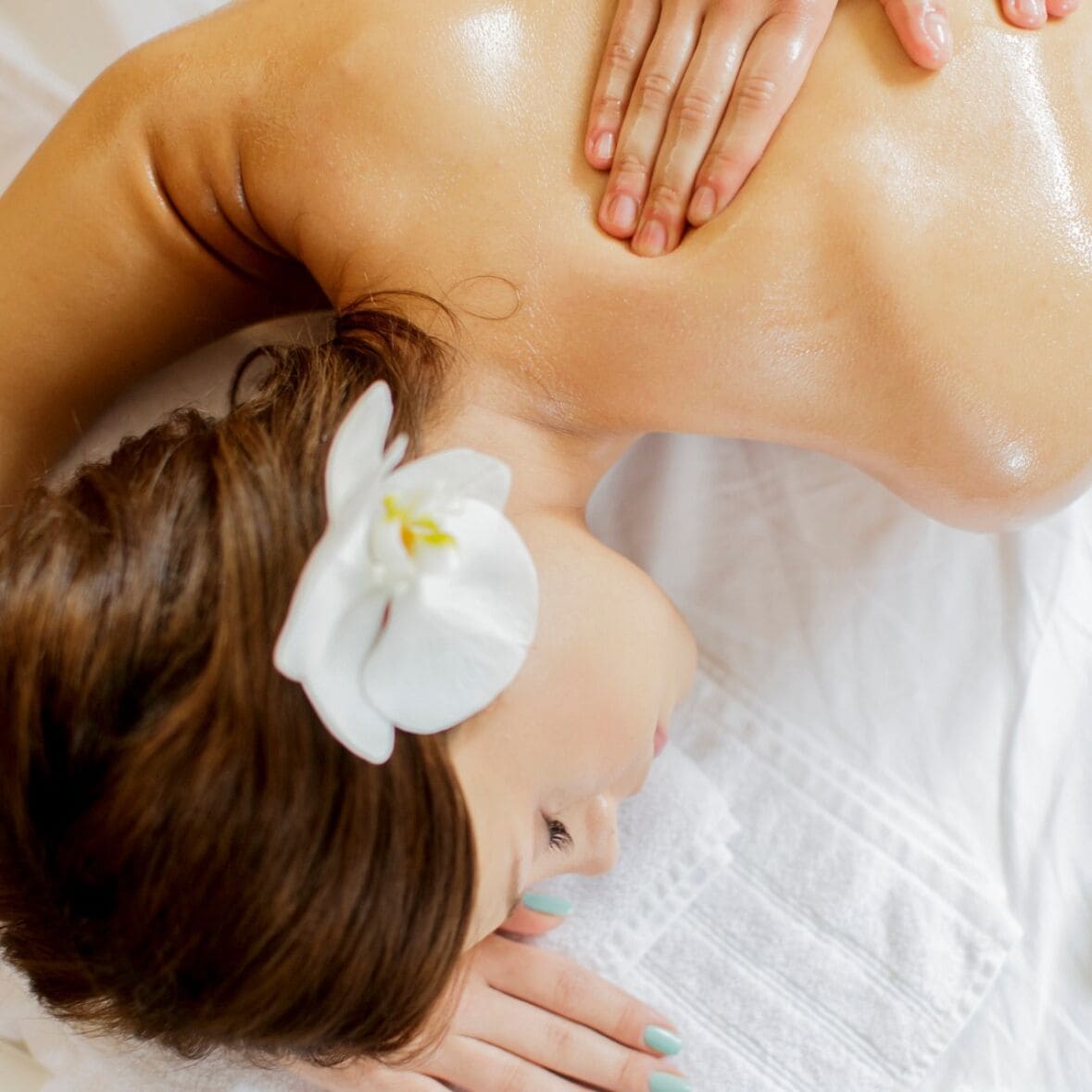 Una persona recostada con una flor en el cabello, evocando un ambiente de spa o relajación.