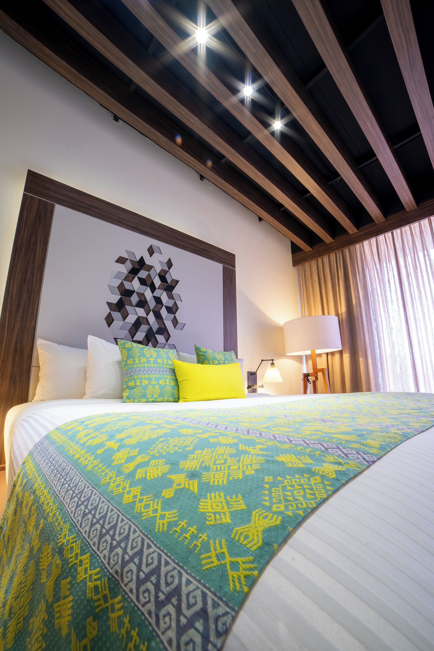 A hotel room with a bed, a wall art piece, a lamp, and a curtain.