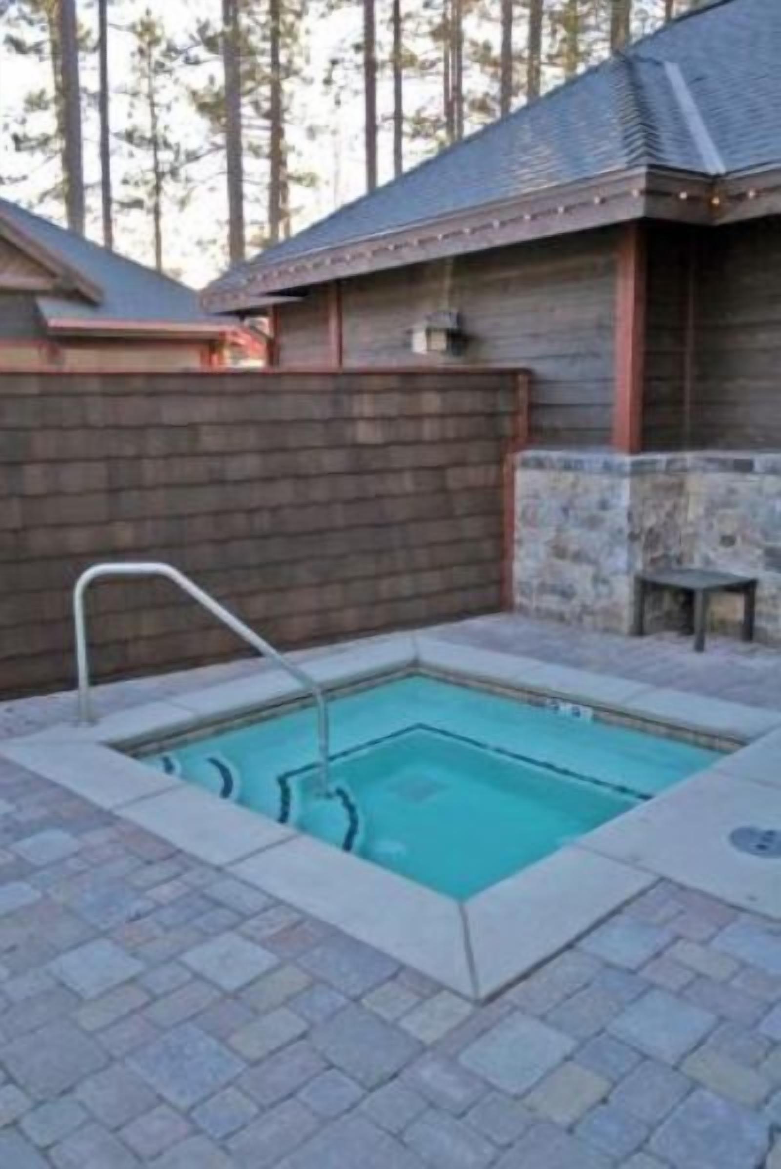 A rectangular pool with a metal ladder, surrounded by a stone and brick patio.
