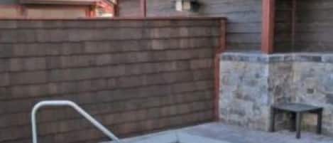 A rectangular pool with a metal ladder, surrounded by a stone and brick patio.