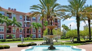 A multi-story hotel with a central fountain surrounded by palm trees and manicured landscaping. - Universal Studio's Area Apt by CozyKey (Orlando)