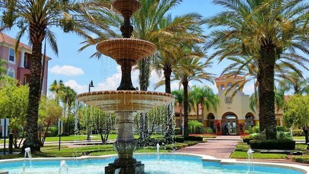 A multi-tiered fountain surrounded by palm trees and a building with arched windows. - Universal Studio's Area Apt by CozyKey (Orlando)