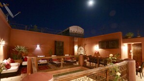 A courtyard with a dining area, a staircase, and a view of the night sky. - Dar Pamella (Marrakech)